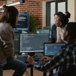 Software developers crowded around a computer with multiple screens looking at coding to represent Azure DevOps