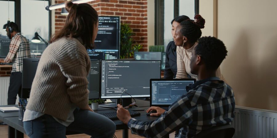 Software developers crowded around a computer with multiple screens looking at coding to represent Azure DevOps