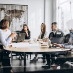 Office works in a meeting room on laptops having a discussion to represent Microsoft Teams custom apps