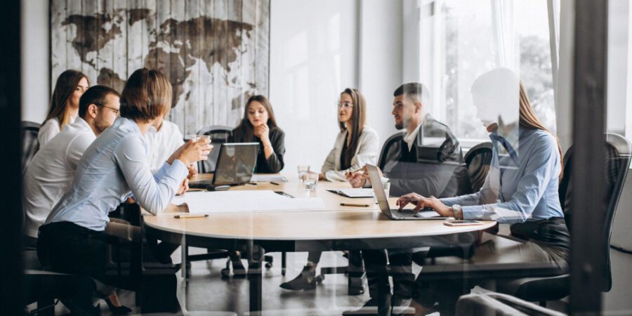 Office works in a meeting room on laptops having a discussion to represent Microsoft Teams custom apps