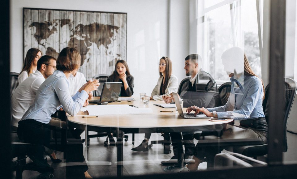 Office works in a meeting room on laptops having a discussion to represent Microsoft Teams custom apps